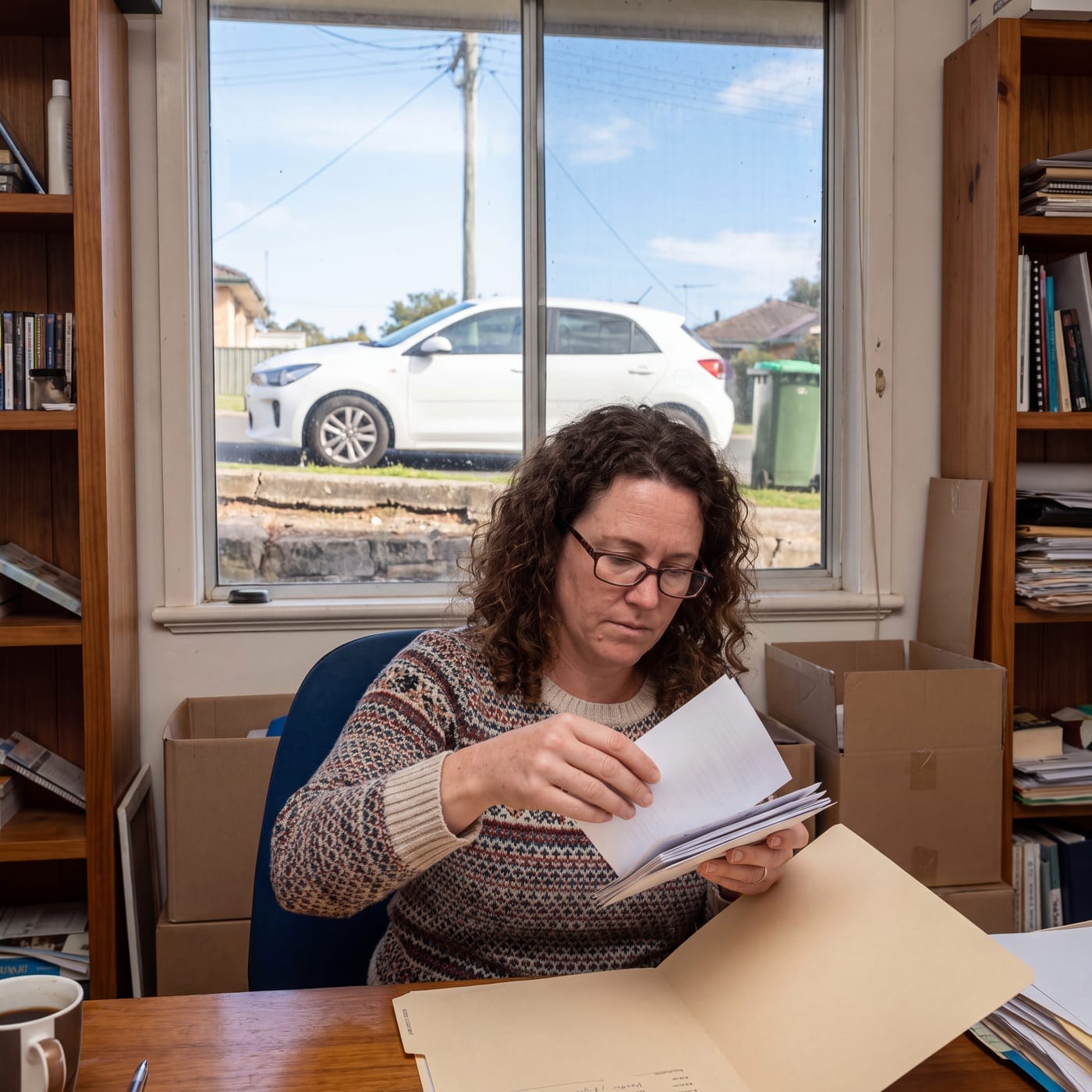 Woman reading through a document at a home office desk beside a window