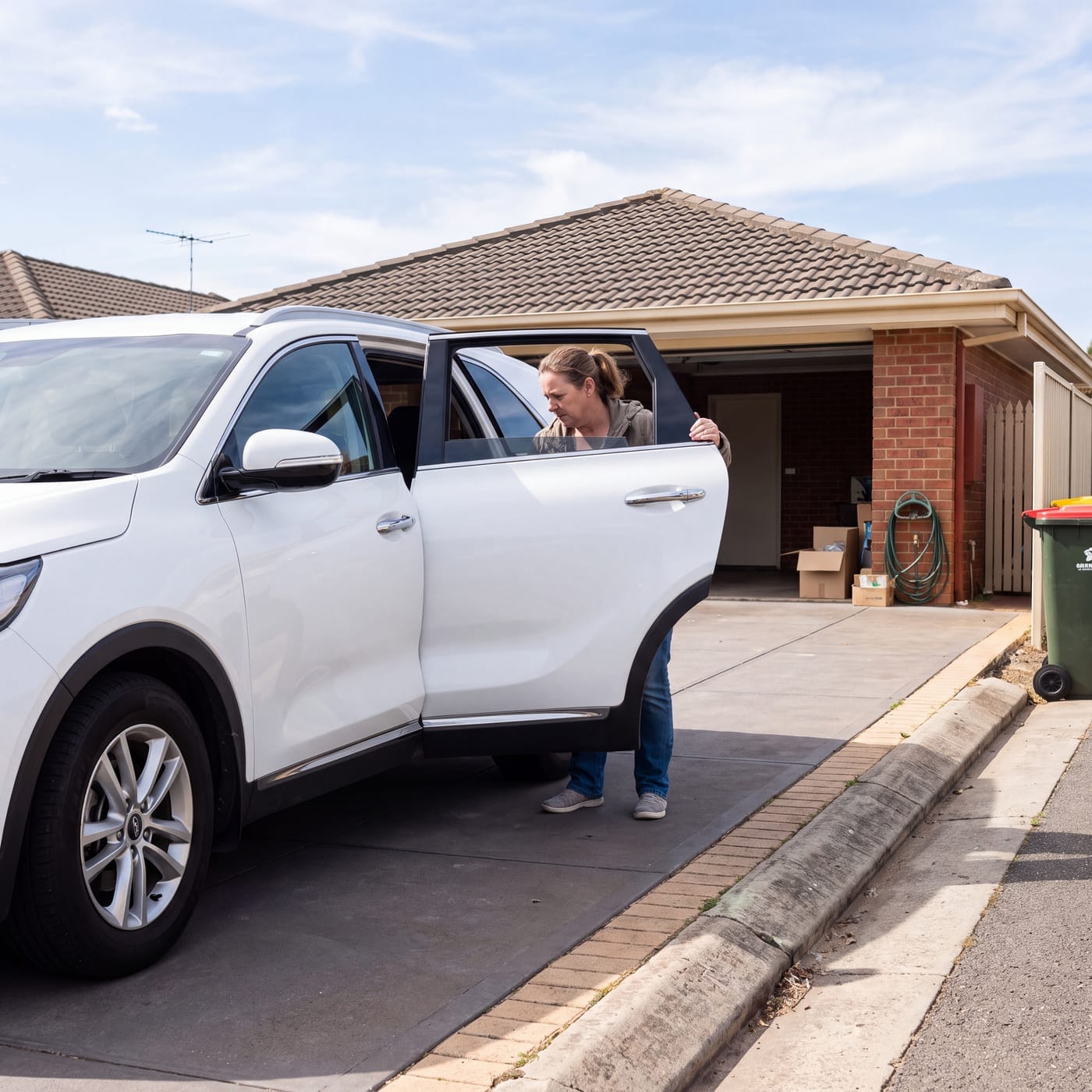 Person reaching into the open door of a vehicle parked in a driveway