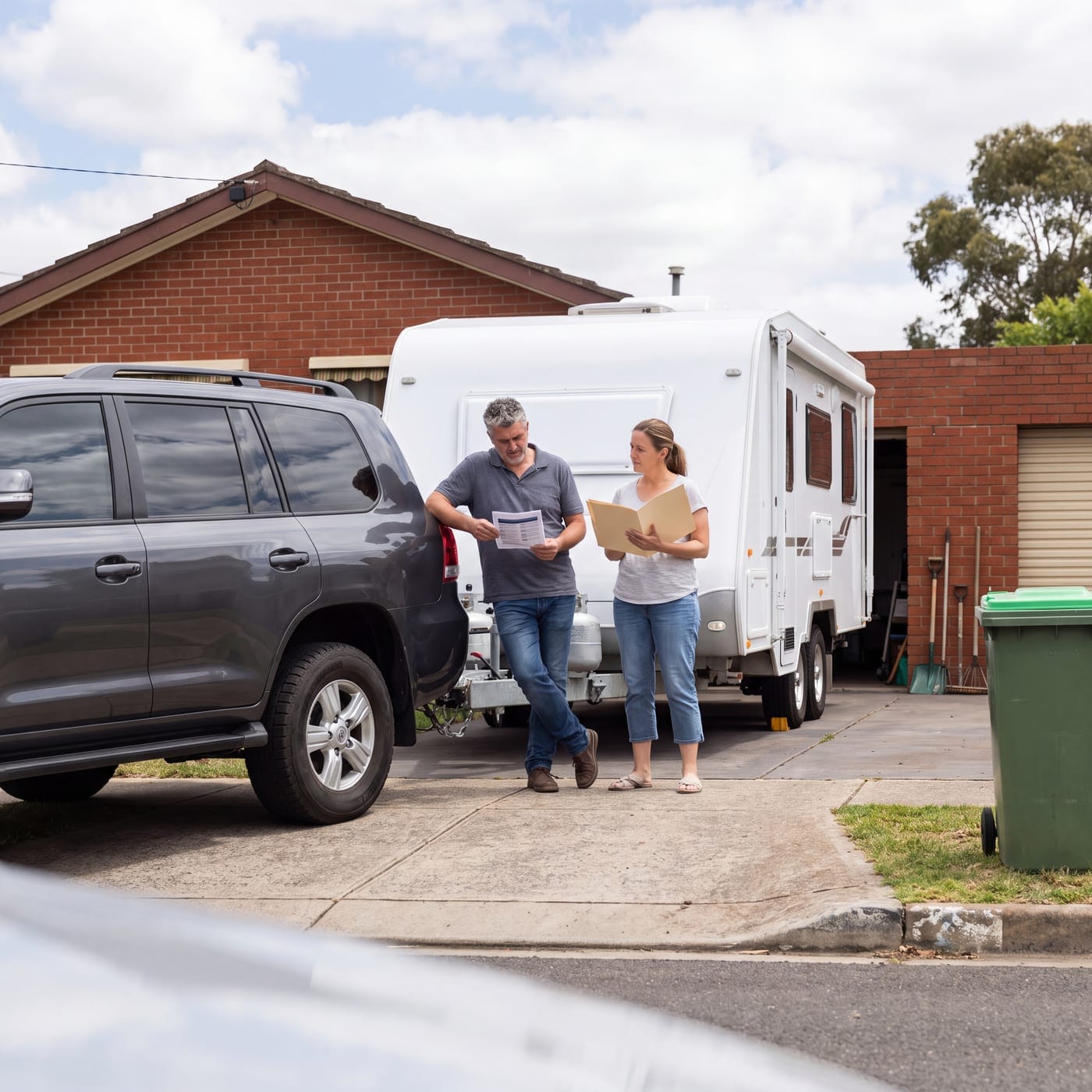 Two people comparing notes in a driveway beside a four wheel drive and a caravan