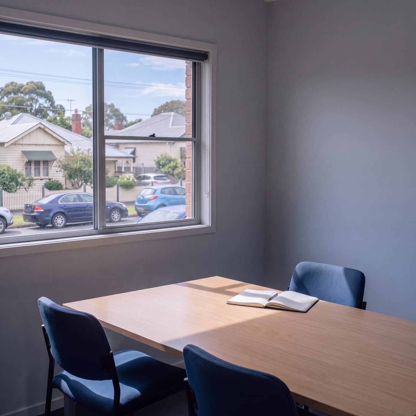 Empty meeting room with a bare table and chairs beside a window onto the street